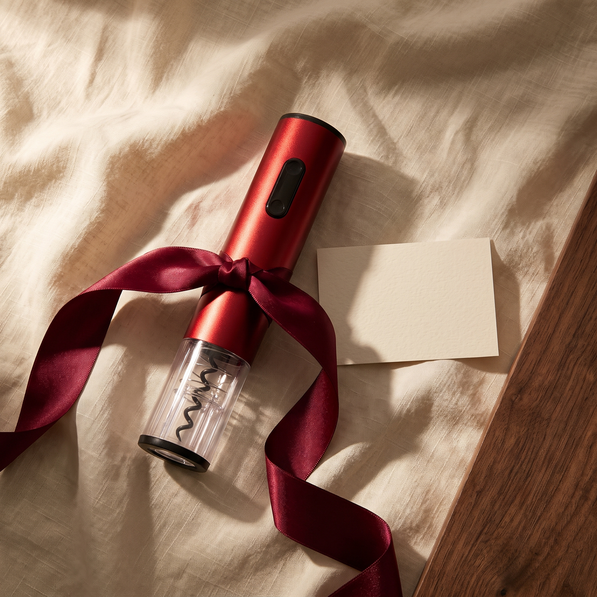 Tire-bouchon électrique rouge présenté en cadeau sur lin avec ruban bordeaux