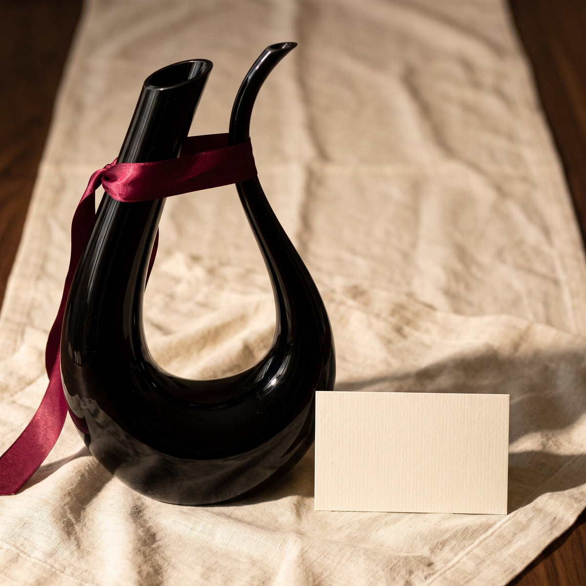 Carafe Black Swan avec ruban cadeau bordeaux sur lin crème