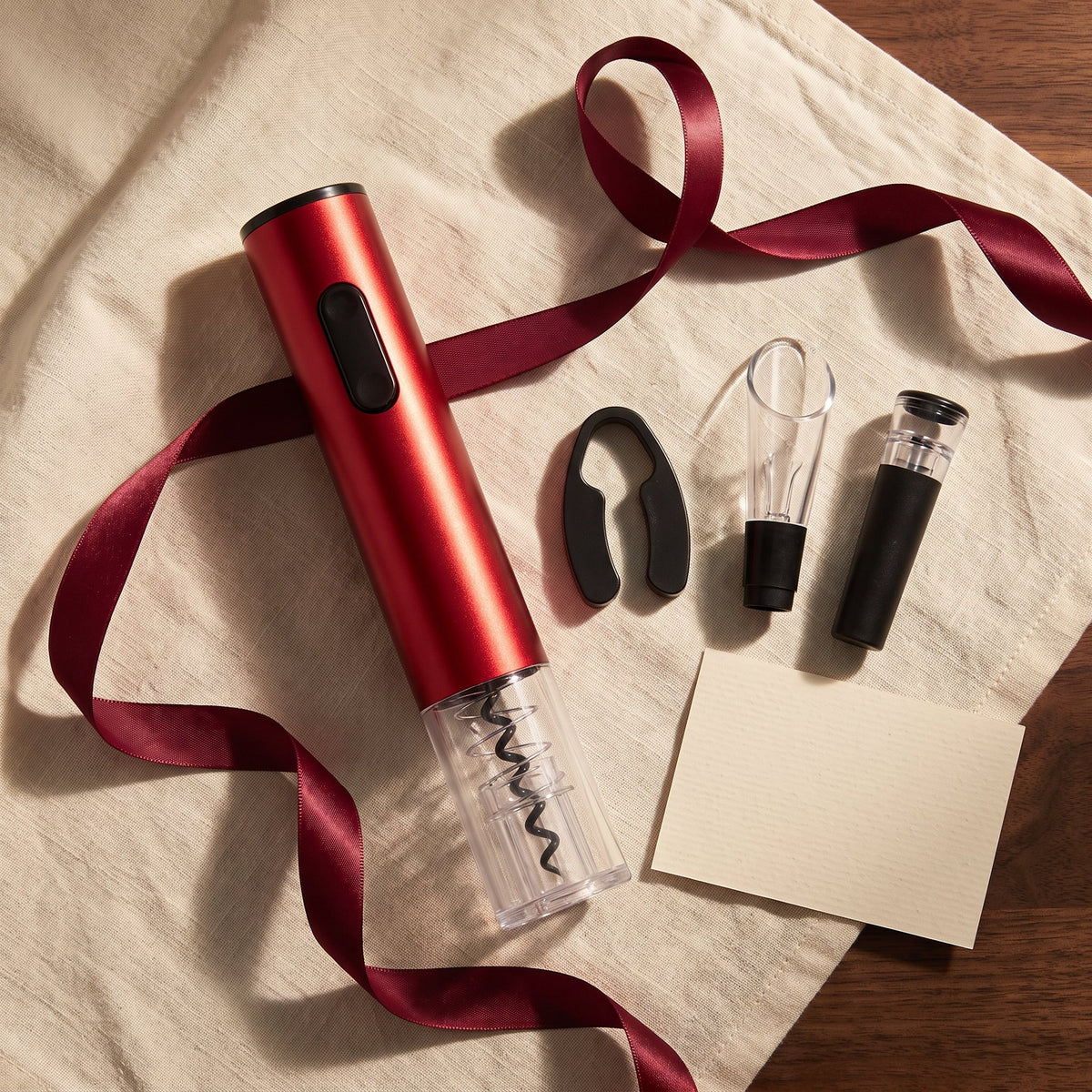 Tire-bouchon électrique rouge et accessoires sur lin crème avec ruban bordeaux, idée cadeau