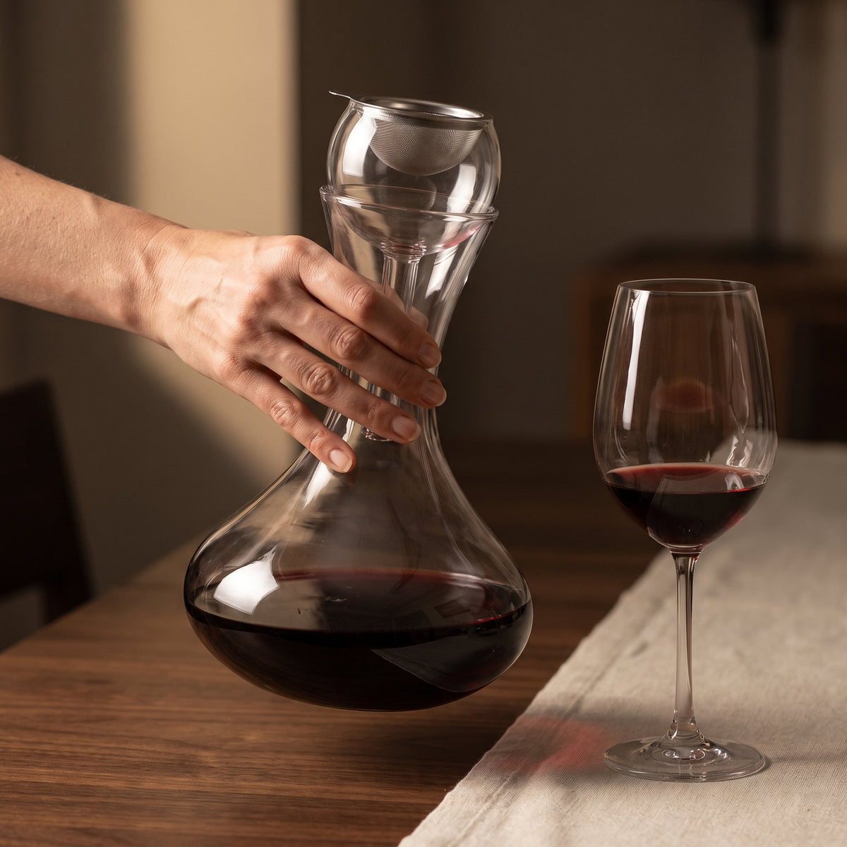 Carafe Nobily tenue en main près d'un verre de vin