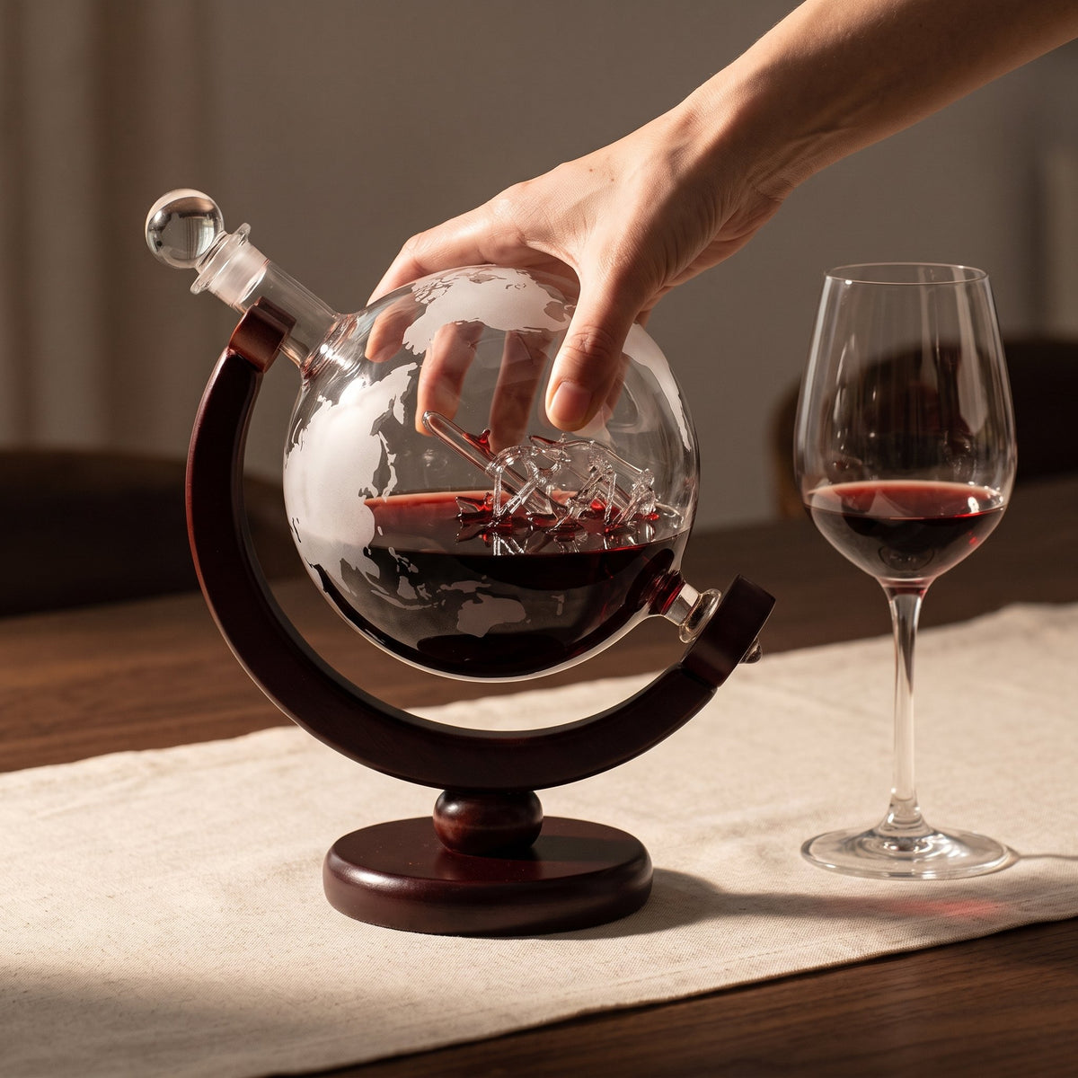 Carafe Globe Trotter tenue en main sur son socle en bois