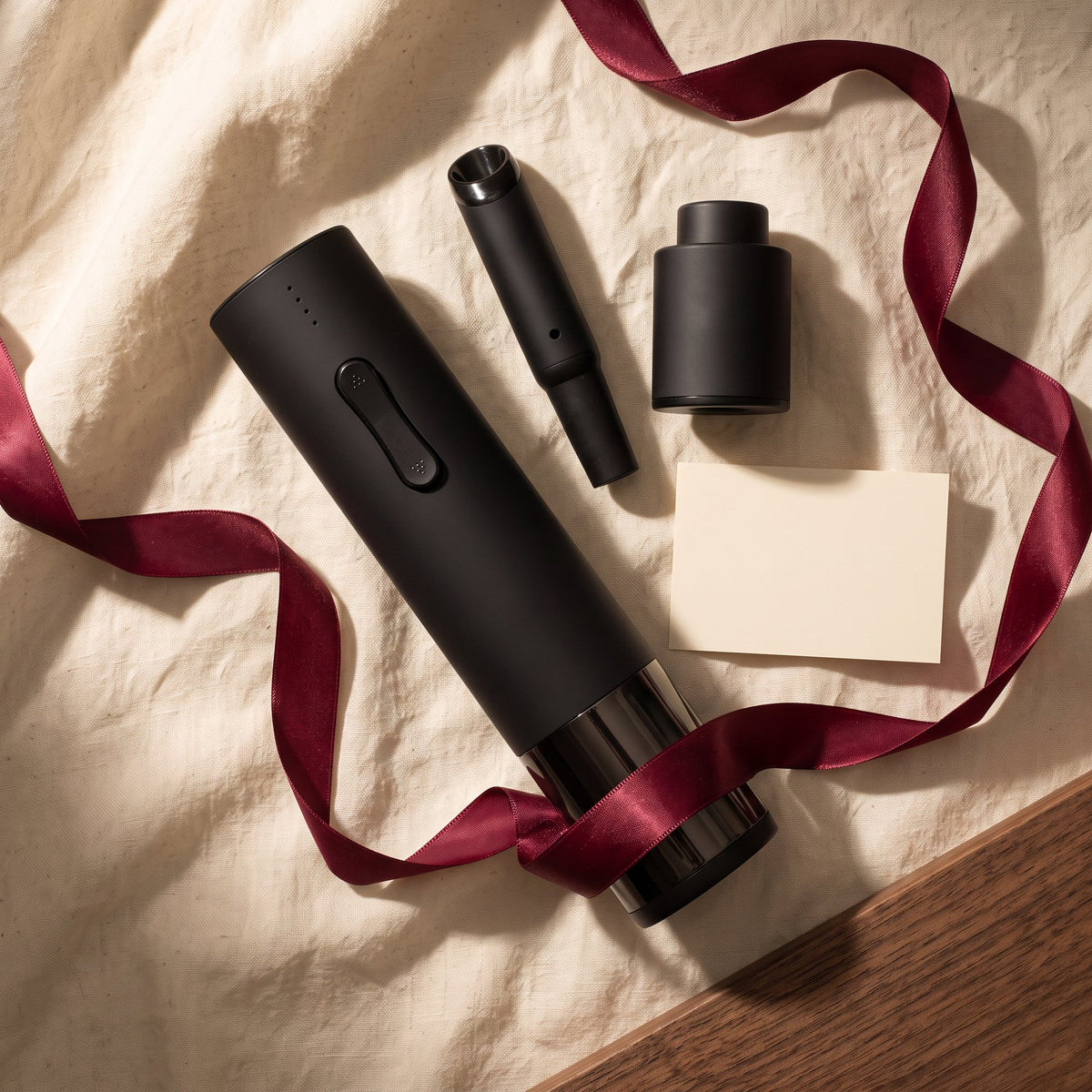 Tire-bouchon électrique noir et accessoires sur lin crème avec ruban bordeaux, idée cadeau