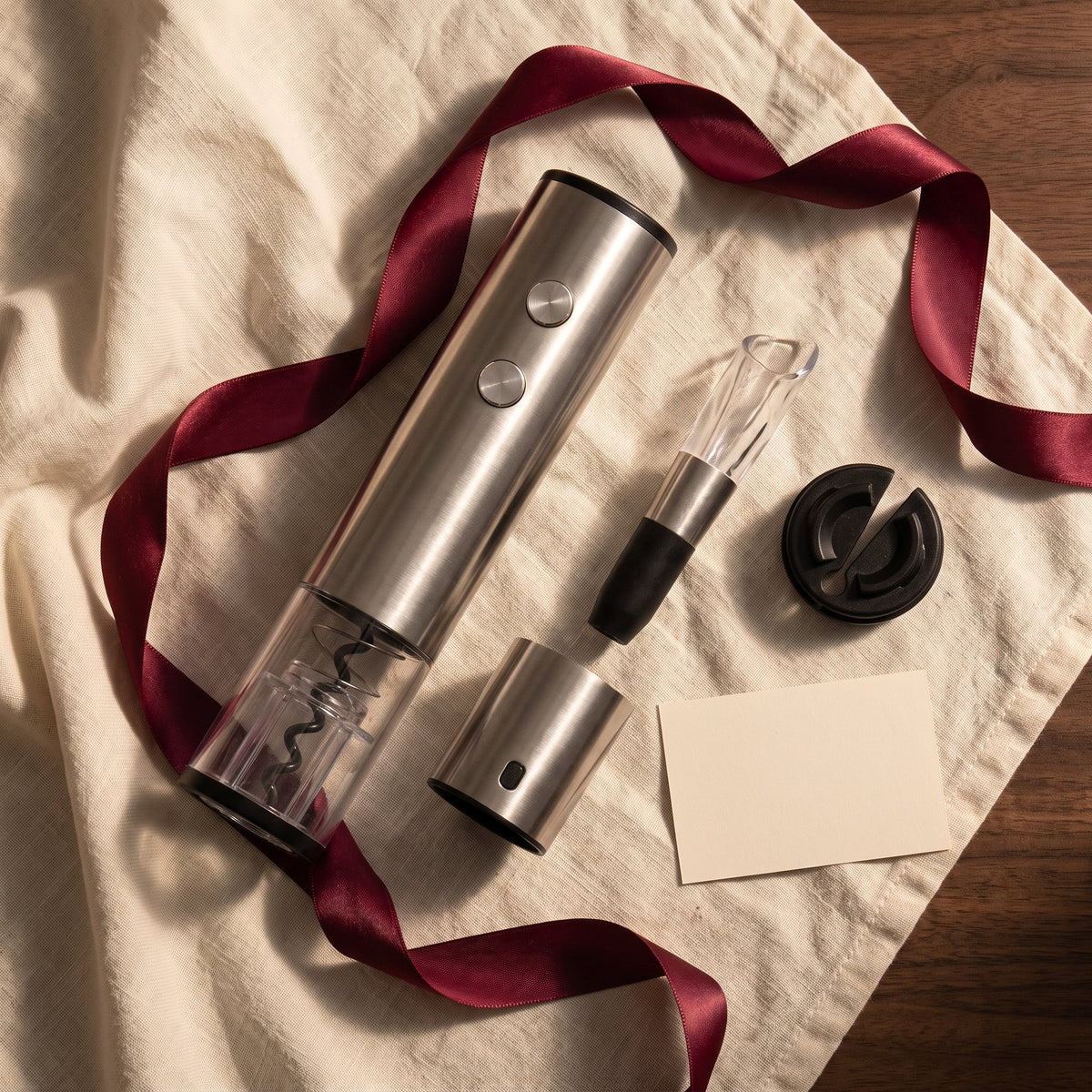 Tire-bouchon électrique et accessoires du pack sur lin crème avec ruban bordeaux, idée cadeau